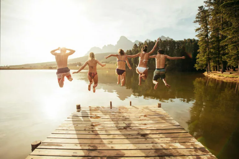 portrait young people jumping from pier into lake together friends jumping off jetty lake sunny day